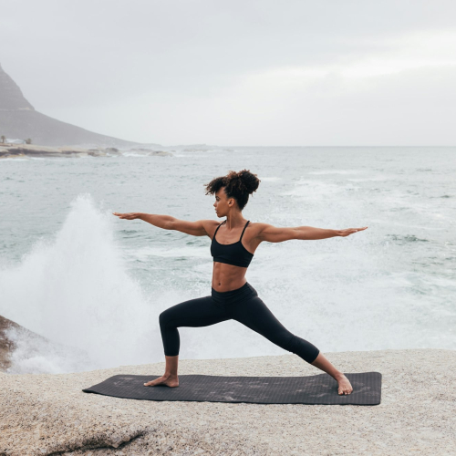 Woman practicing warrior yoga pose against big waves and an ocean