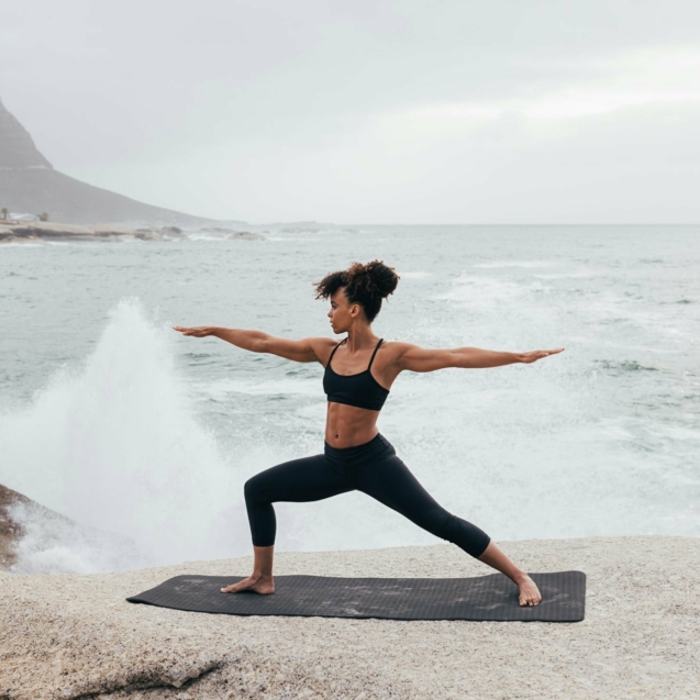 Woman practicing warrior yoga pose against big waves and an ocean